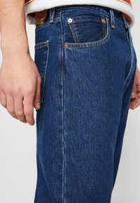 Vaqueros de mezclilla azul oscuro con corte recto. Presentan costuras sutiles, cinco bolsillos, remaches de cobre y una textura suave.