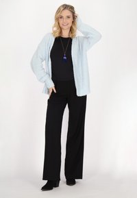 Cardigan peluche azzurro, body nero e pantaloni larghi neri. L'outfit è completato da una lunga collana con un pon-pon blu.