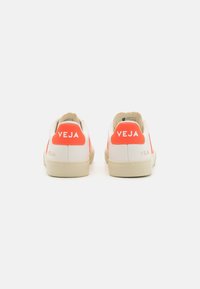 Hvite lær sneakers med lyse korallfarger, som har et lavt design, teksturert hæl og synlig merkevarelogo bak.