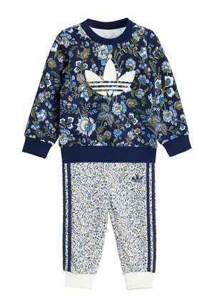Sweatshirt floral marine avec logo Adidas blanc, assorti à un pantalon blanc à motifs avec des accents bleus et des rayures marines. Tissu doux.
