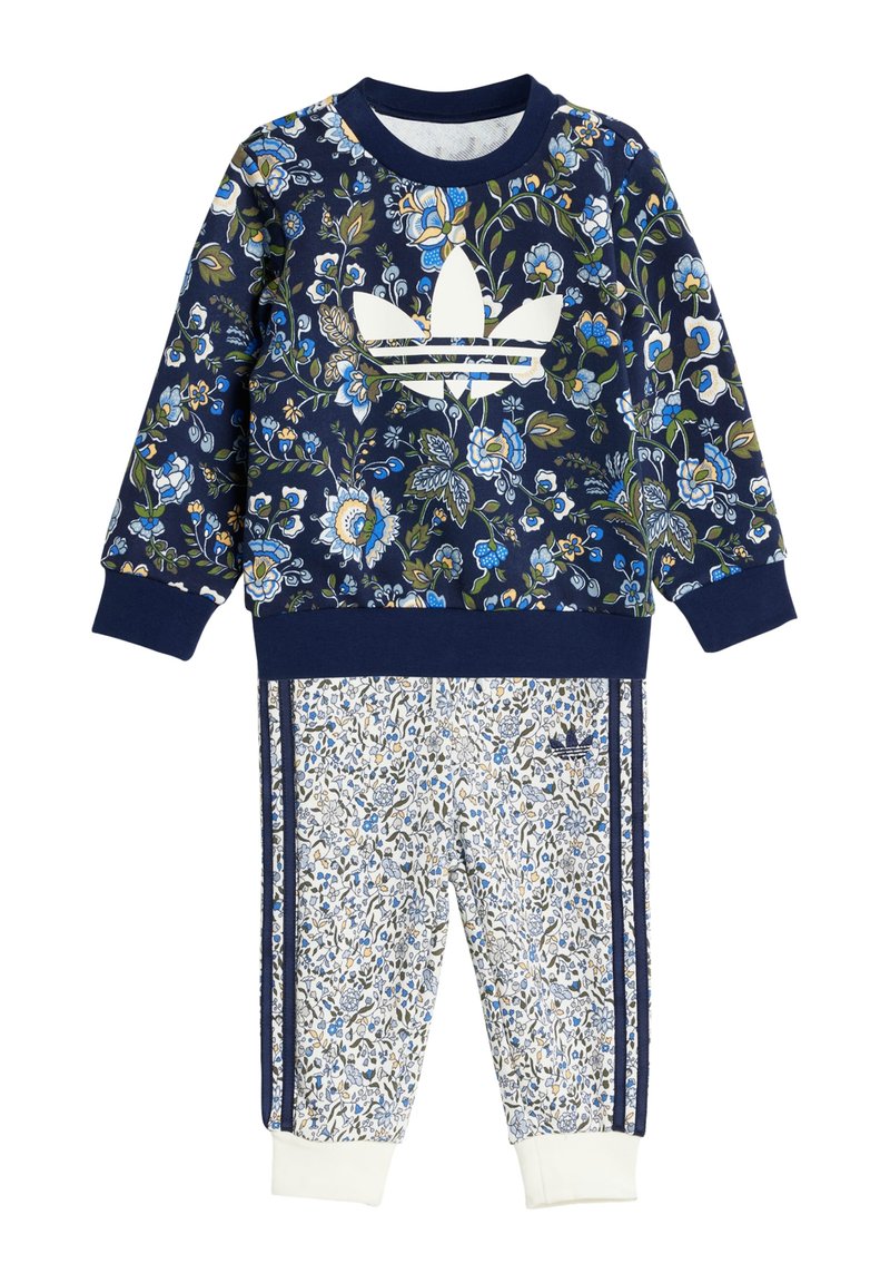 Jūrinės gėlės motyvo džemperis su baltu Adidas logotipu, derinamas su raštuotomis baltomis kelnėmis, turinčiomis mėlynus akcentus ir jūrinius dryžius. Minkšta medžiaga.