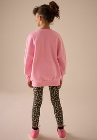 Lyserød oversized sweatshirt, leggings med leopardprint og lyserøde sneakers. Materialet fremstår blødt. Designet har rund hals og lange ærmer.