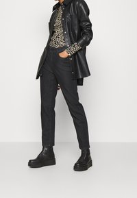 Czarny skórzany płaszcz z srebrnymi napami na beżowej, czarnej bluzce w leopardzie wzory. Czarne slim-fit spodnie i masywne czarne sznurowane botki.