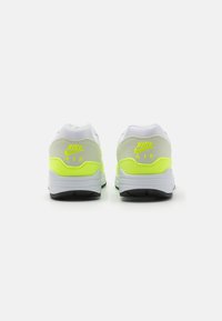 Adidași Nike Air, cu un aspect superior alb, accente gri și galben neon, talpă din cauciuc texturat și detaliu cu logo pe toc.