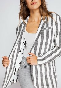 Striped blazer in black and white linen, featuring a single breast pocket and a contrasting patterned interior, styled with a plain white tank.