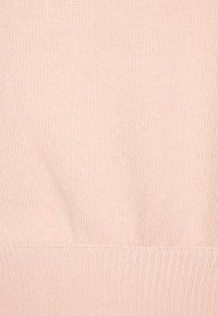 Ljusrosa stickad tröja med en mjuk struktur, ribbade ärmslut och nederkant samt en slät yta. Designen betonar enkelhet och komfort.
