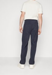 Dunkelblaue Cordhosen mit geradem Schnitt, elastischem Bund und einer Gesäßtasche. Kombiniert mit einem hellbeigen T-Shirt und weißen Sneakers.