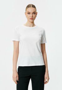 Witte katoenen t-shirt met korte mouwen, ronde hals en subtiele "ATTITUDE" tekst gedrukt op de voorkant. Gladde textuur en aansluitend ontwerp.