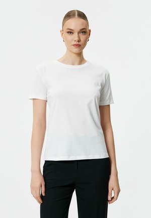 Hvid bomulds t-shirt med korte ærmer, rund halsudskæring og diskret "ATTITUDE" tekst trykt på forsiden. Glat tekstur og tætsiddende design.