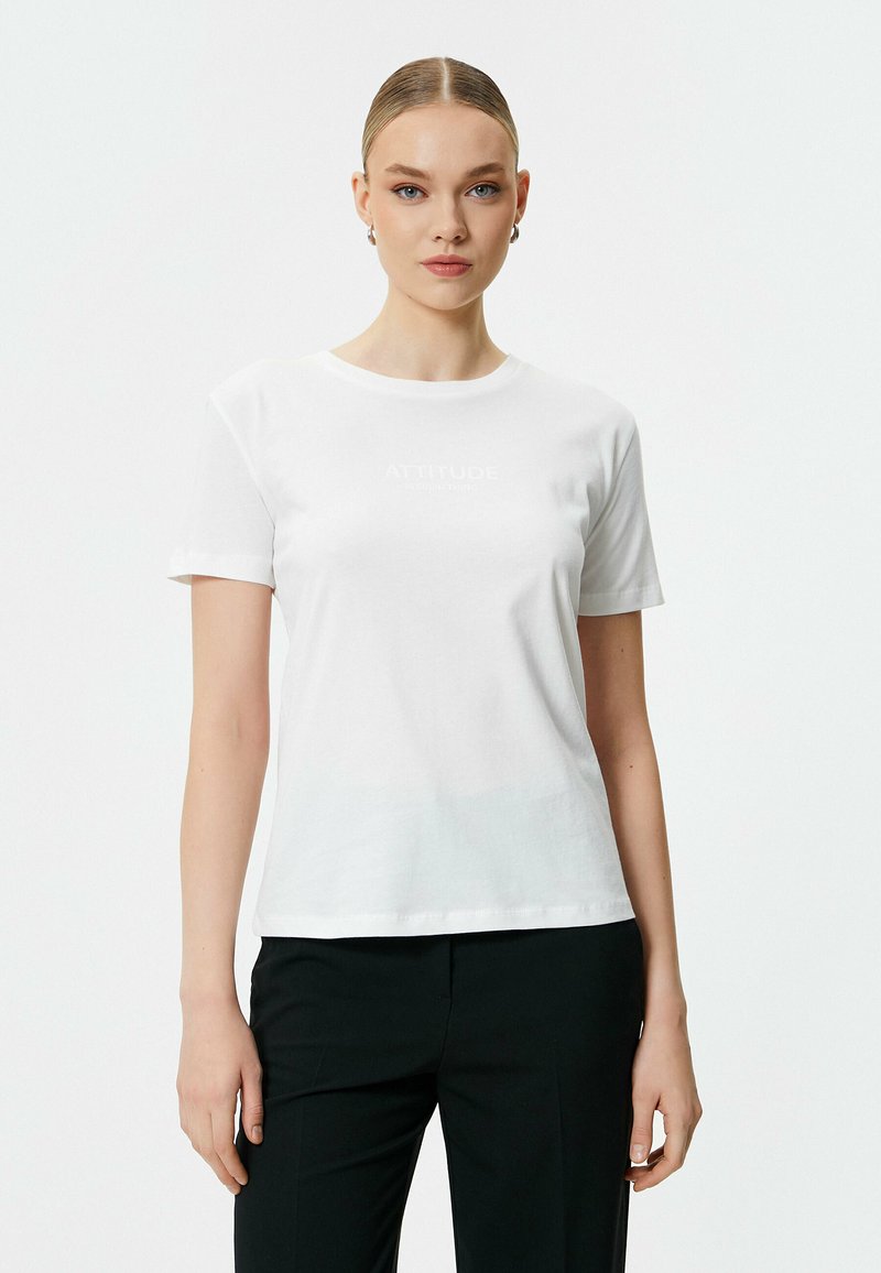 Witte katoenen t-shirt met korte mouwen, ronde hals en subtiele "ATTITUDE" tekst gedrukt op de voorkant. Gladde textuur en aansluitend ontwerp.