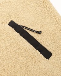 Tan fleece-stoff med en teksturert overflate, med en svart lomme i stoff med snor for ekstra kontrast.