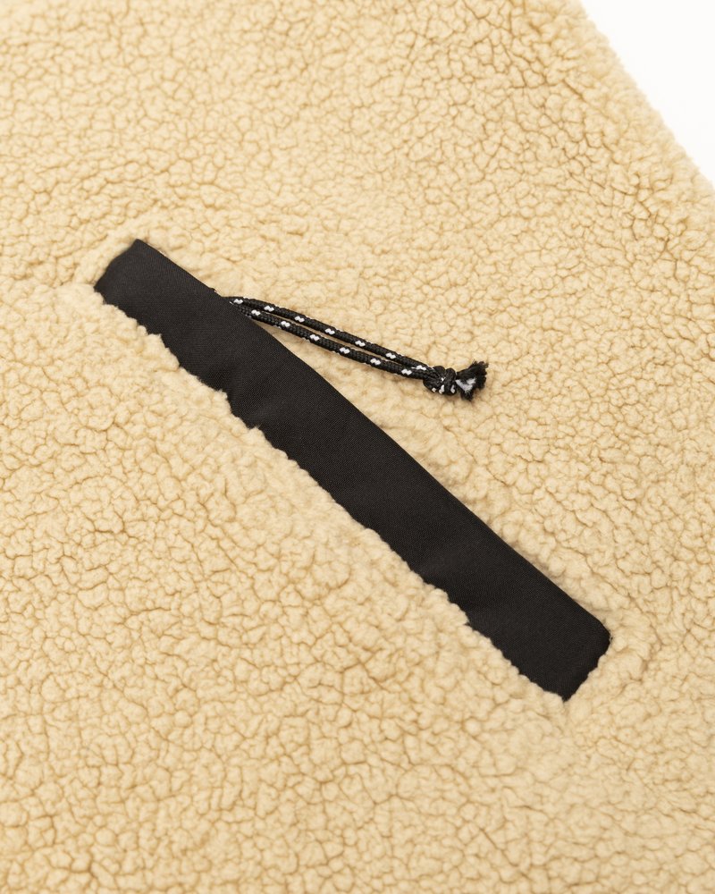 Tissu en polaire beige avec une surface texturée, présentant une poche en tissu noir avec un détail de cordon pour un contraste supplémentaire.