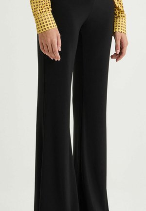 Pantaloni neri a zampa con una texture liscia, dotati di una vita aderente, abbinati a un top giallo a maniche lunghe con un motivo circolare.