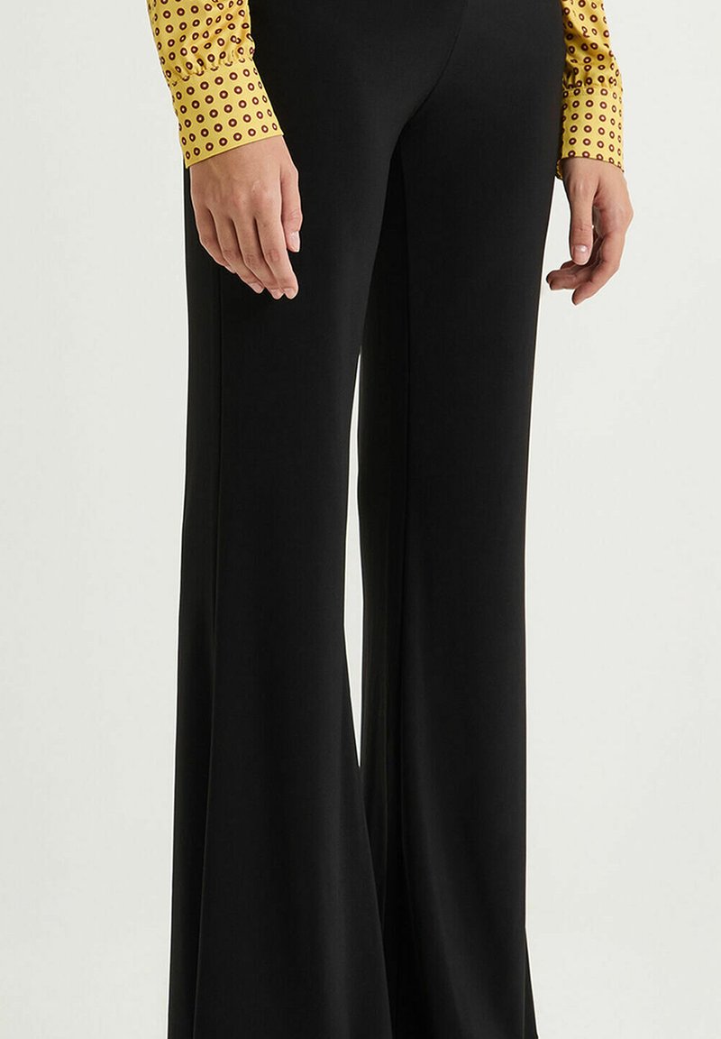 Pantalon noir évasé avec une texture lisse, doté d'une taille ajustée, accompagné d'un haut jaune à manches longues avec un motif circulaire.