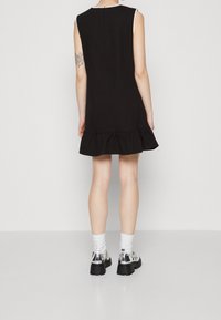 Vestito nero senza maniche con orlo a sbuffo, realizzato in un tessuto liscio. Indossato con scarpe metalliche e calzini bianchi, caratterizzato da un design semplice.