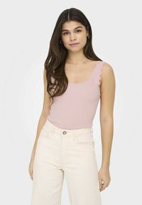 Top de tirantes acanalado de color rosa claro con bordes festoneados, combinado con vaqueros de cintura alta en color blanco roto. Diseño sencillo y ajustado.