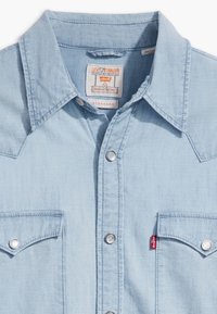 Lys blå denim westernskjorte med spiss krage, trykknapp-lukking og to brystlommer. Har Levi's-merke på venstre lomme.