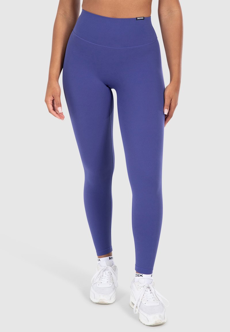Hoge taille, effen paarse leggings gemaakt van rekbaar materiaal. Glad textuur met platte naden, gedragen met witte sportschoenen.