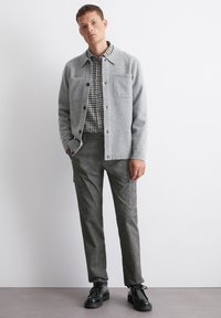 Gray wool-blend jacket with two chest pockets layered over a black and white gingham shirt; paired with gray cargo-style pants and black shoes.
