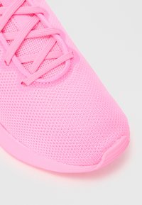 Roze sportieve schoen met een geperforeerde mesh bovenkant, voorzien van bijpassende veters en een gladde rubberen zool met een lichte kromming bij de teen.