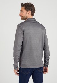 Grijze lange mouwen shirt met een zachte textuur en een simpele kraag, voorzien van knoopmanchetten en een klein logo aan de zoom.