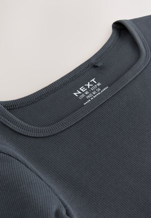 Tamnosivi rebrasti top s okruglim izrezom i vidljivom etiketom s uputama za njegu. Glatka tekstura s diskretnim detaljima šavova.