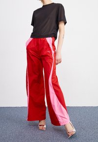 Pantalons de jogging rouges et roses à jambes larges avec une taille élastique, arborant un logo Puma. Associés à un t-shirt noir transparent.