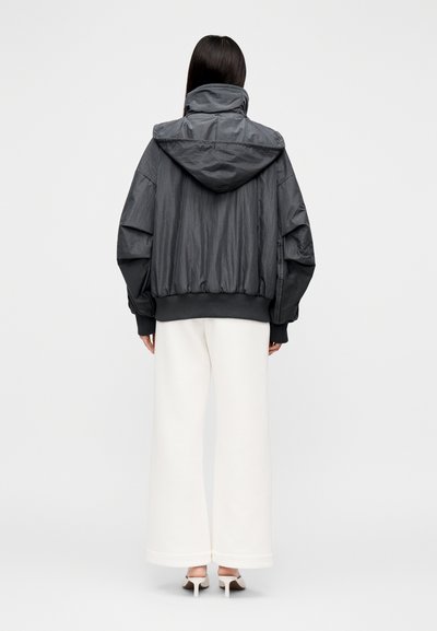 Pilka gobtuvu pasiūta bombonešio striukė su elastinėmis rankogaliais ir apačia, derinama su baltomis plačiomis kelnėmis, matoma iš nugaros.