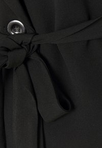 Zwarte stof met een ceintuur die in de taille is geknoopt, voorzien van een decoratieve knoopdetail, met een gladde, gestructureerde uitstraling.