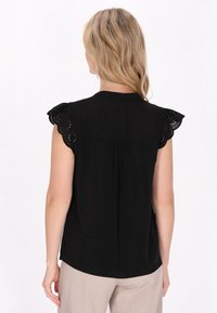 Blusa nera con maniche corte a occhiello smerlato, schiena plissettata e orlo leggermente curvato, realizzata in tessuto leggero.