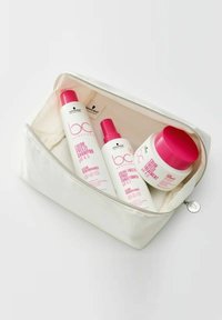 Vit kosmetisk väska med dragkedja som innehåller tre hårvårdsprodukter: schampo, balsam och behandling, alla med rosa accenter och etiketter.