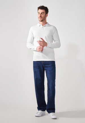 Witte lange mouwen polo met kraag, gecombineerd met een blauwe denim jeans en witte sneakers. Het shirt heeft een gladde textuur en een slimfit vorm.