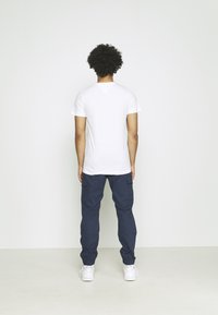 Bílé tričko s krátkými rukávy a tmavě modré kapsáčové kalhoty s elastickými manžetami, s bočními kapsami a rovný střihem, nošené s bílými teniskami.