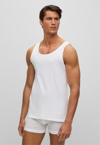 Débardeur en coton blanc avec un col rond, doté de larges bretelles. Associé à un short boxeur blanc, en tissu lisse et au design ajusté.