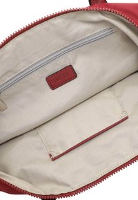 Interno di una borsa rossa con zip, foderato in tessuto chiaro, con una tasca con zip e un compartimento piatto. Il materiale è liscio con un design strutturato.