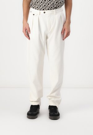 Pantaloni plisati albi din bumbac, cu talie înaltă, buzunare laterale și croi lejer, asortați cu adidași negri.