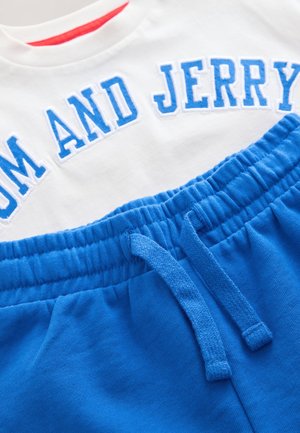 Maglietta bianca con la scritta "TOM AND JERRY" in lettere blu, abbinata a pantaloncini in cotone blu con vita elasticizzata e coulisse.