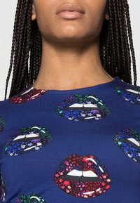 Blue short-sleeve top featuring a pattern of colorful lips, detailed with floral designs and glossy accents. Soft fabric with a smooth texture.