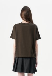 Brown short-sleeve t-shirt with a crew neck, relaxed fit, smooth texture, and straight hem, paired with a pleated black skirt.