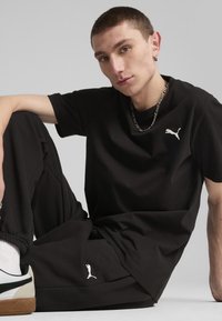 Zwarte T-shirt met korte mouwen en relaxed-fit broek, beide met een klein wit Puma-logo. De stof lijkt glad en de pasvorm is iets losser.