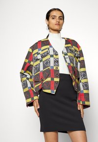 Bunte karierte Jacke in Gelb, Rot und Grau mit Tiermotiven, oversized Schnitt und Fronttaschen, kombiniert mit einem schwarzen Bleistiftrock.