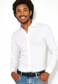 Witte lange mouwen overhemd met een button-down kraag, slank pasvorm ontwerp, zachte textuur, gecombineerd met blauwe denim jeans en een zwarte gevlochten riem.