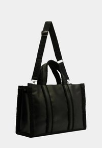 Sac fourre-tout noir avec un corps en cuir lisse et des côtés en textile moelleux. Doté de deux anses pour l'épaule et d'une forme rectangulaire structurée.