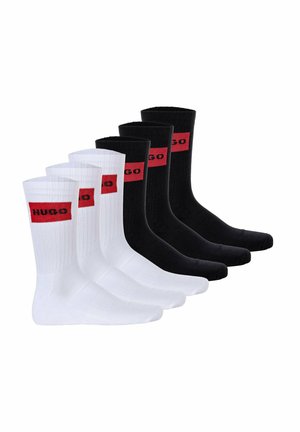 Drei Paar Crew-Socken: zwei weiße und ein schwarzes Paar. Jede hat eine gerippte Struktur mit einem roten "HUGO"-Logo-Band am oberen Rand.