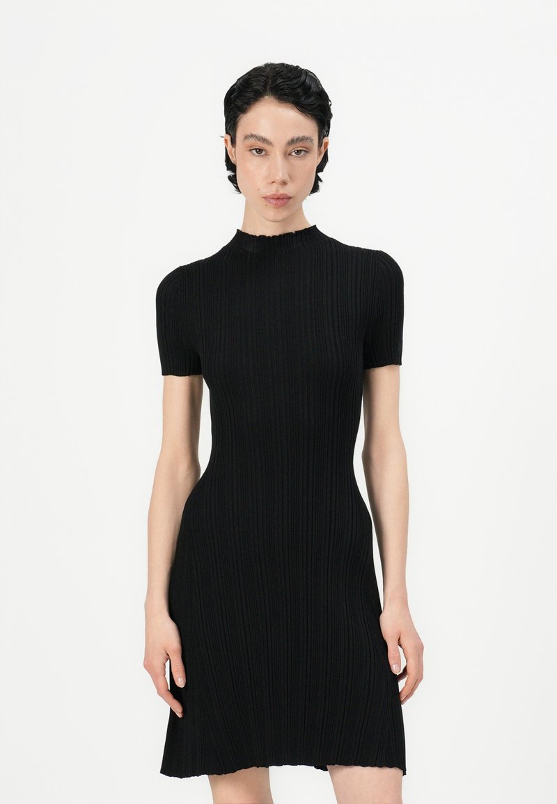 Black ribbed knit dress with short sleeves, high neckline, and a fitted silhouette. Features a flared hem with a raw edge.