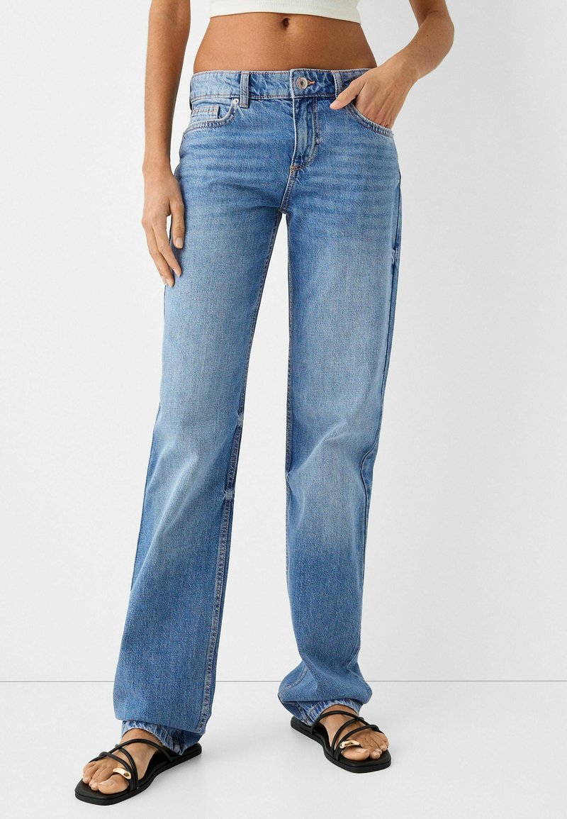 Jeans de denim azul claro con corte recto, cinco bolsillos y un ligero desgastado. Cuenta con un cierre de botón y cremallera, además de una cinturilla con trabillas.