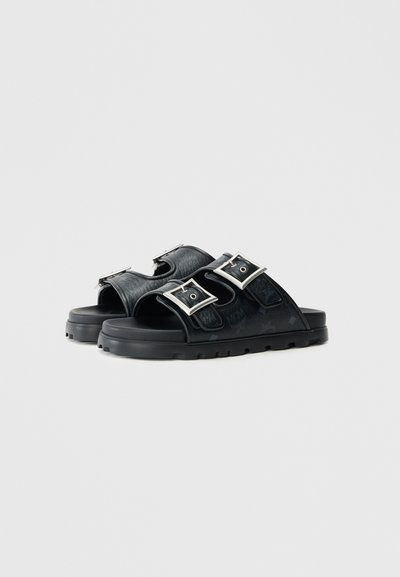 Sorte sandaler med to spænderemmer, lavet af struktureret syntetisk materiale, med en formet sål og mønstrede detaljer på overdelen.