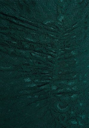 Tessuto di pizzo verde scuro con motivi floreali intricati e un sottile luccichio, che mostra dettagli di trama arricciata e raccolta.