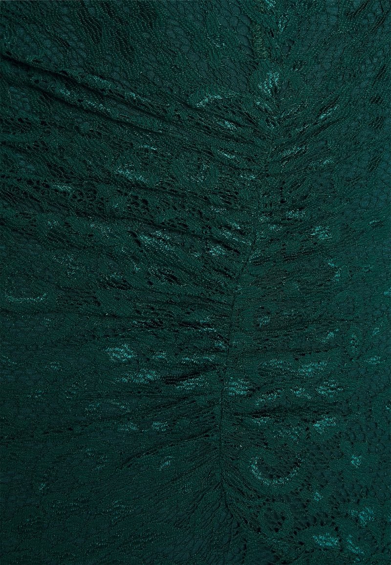 Tissu en dentelle vert foncé avec des motifs floraux complexes et un subtil scintillement, montrant des détails de texture froncée et plissée.