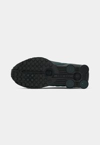 Sola de borracha preta de um sapato Nike Shox exibindo manchas circulares e o logótipo "Nike Shox" no centro.